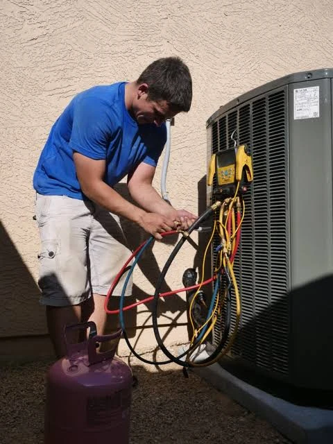 HVAC technician servicing an outdoor air conditioning unit with refrigerant gauges