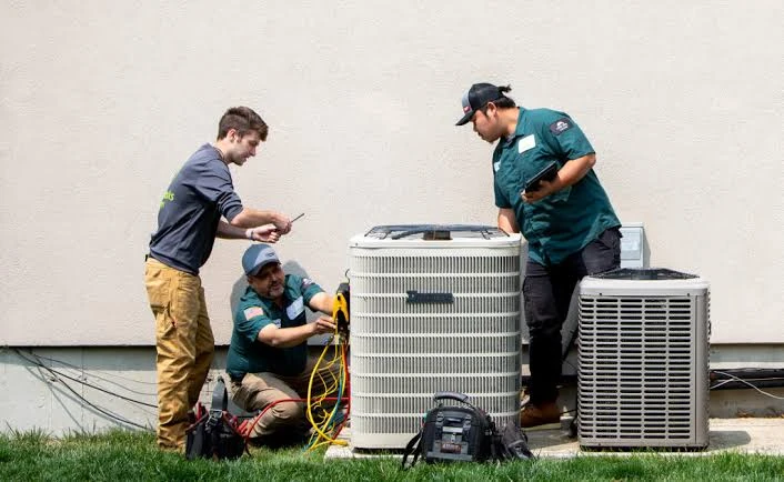 Three technicians inspecting outdoor residential heating and cooling equipment
